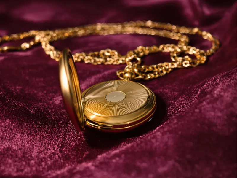 A brass pocket watch lying case-back up on velvet, its lid open and its chain coiled beside it