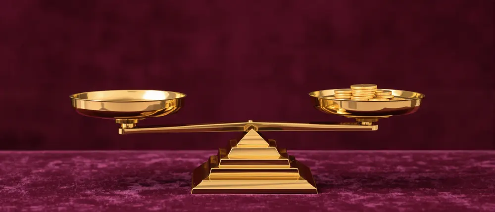 A brass art deco balance scale holding coins on plum velvet